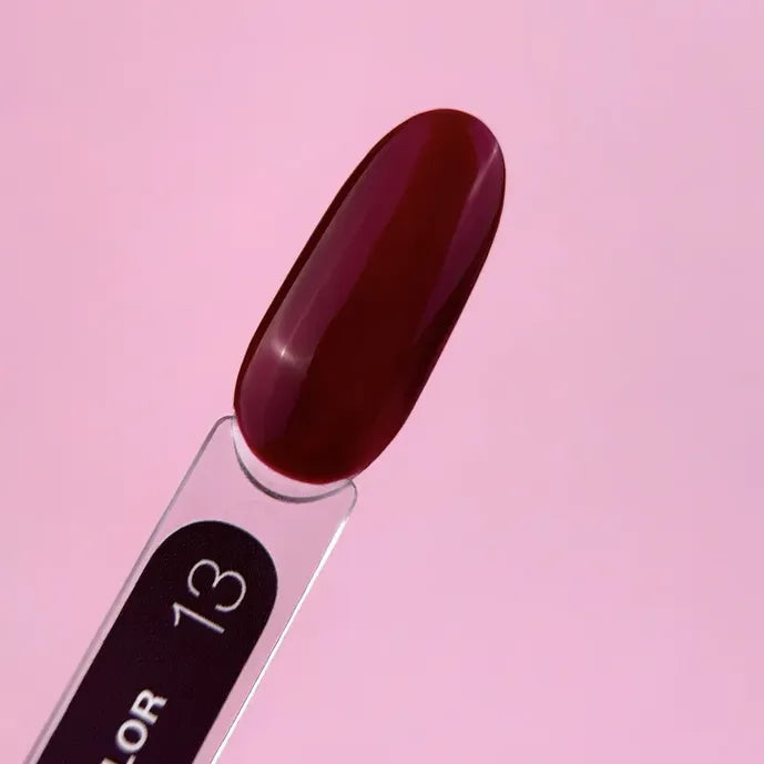 Deep burgundy gel nail polish swatch on clear stick against pink background