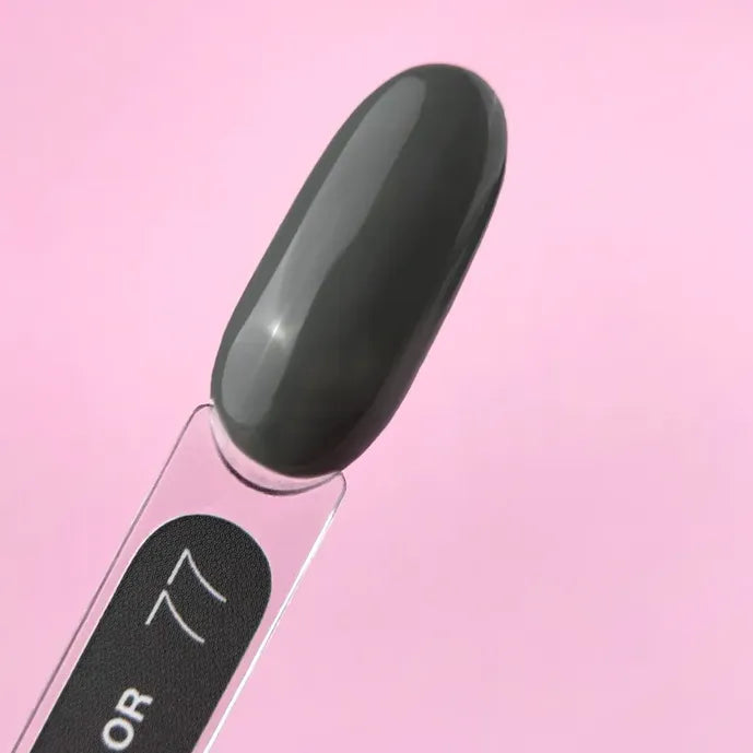 Black gel nail polish swatch on clear stick against pink background, professional manicure demo