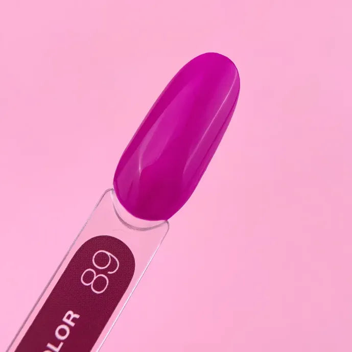 Swatch of bright magenta gel nail polish on display stick, pink background