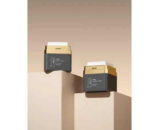 Two black and gold 30ml nail gel bottles on beige pedestals with a neutral background