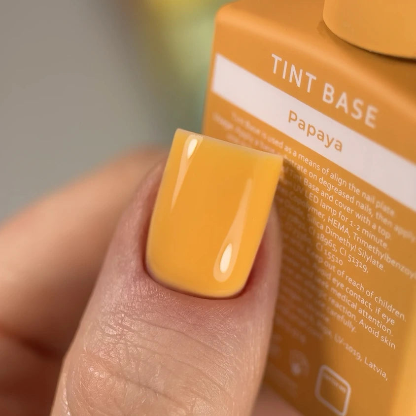 Close-up of a fingernail with glossy papaya orange gel polish, holding a Tint Base bottle.