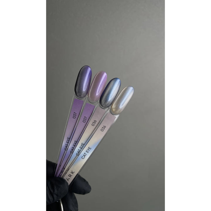 Four cat eye gel nail polish sample sticks in metallic purple and silver shades, held by a gloved hand