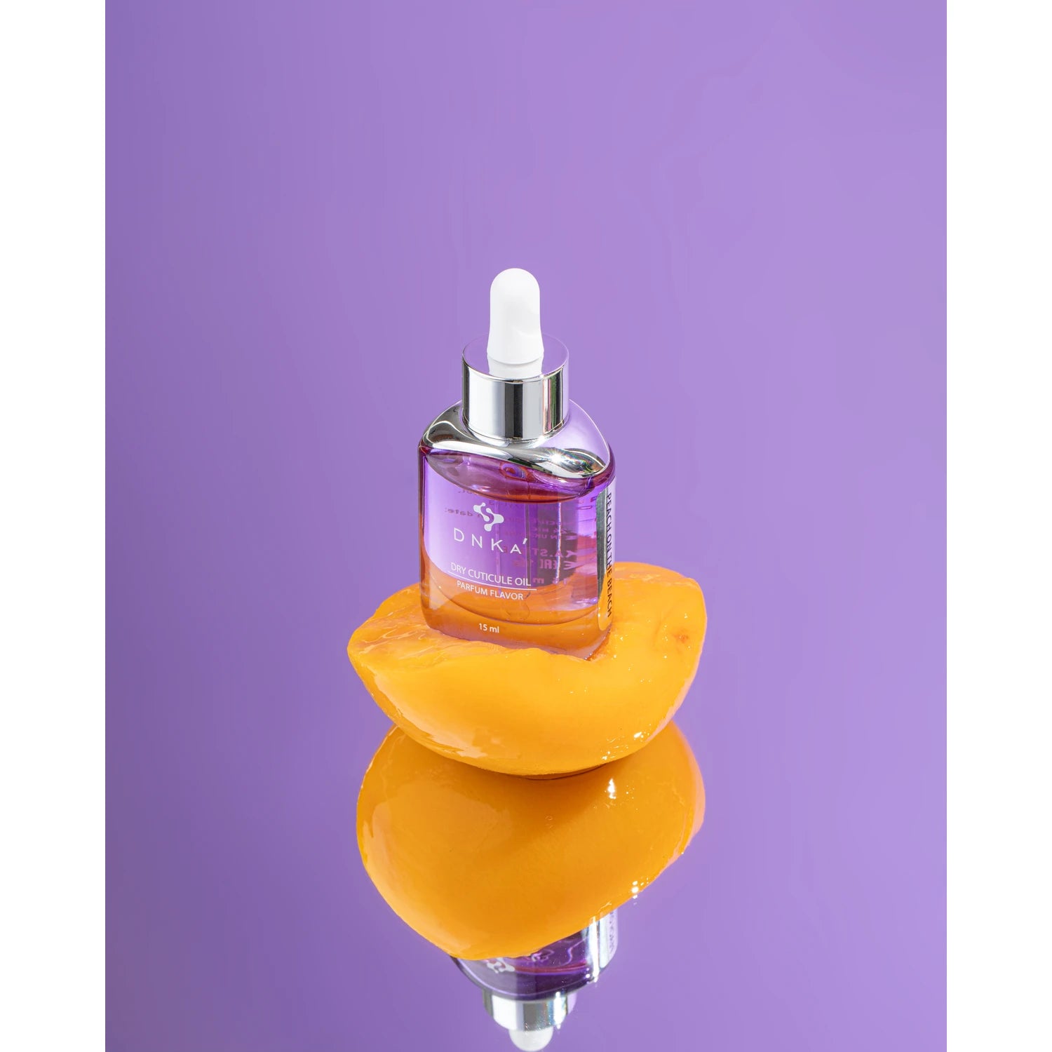 DNKA dry cuticle oil in glass dropper bottle on peach slice, purple background