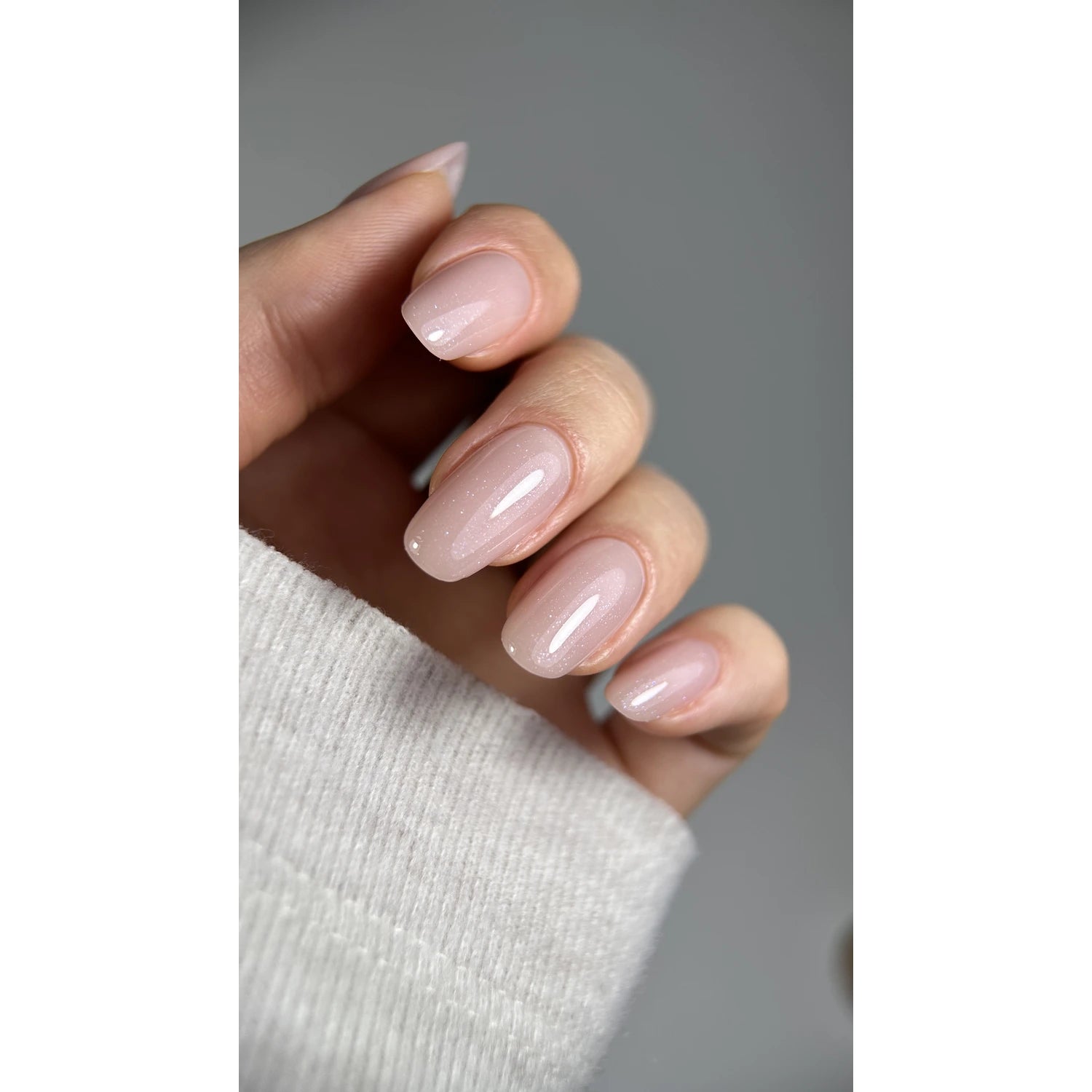 Hand with short oval nails in light pink UV gel polish, glossy manicure close-up