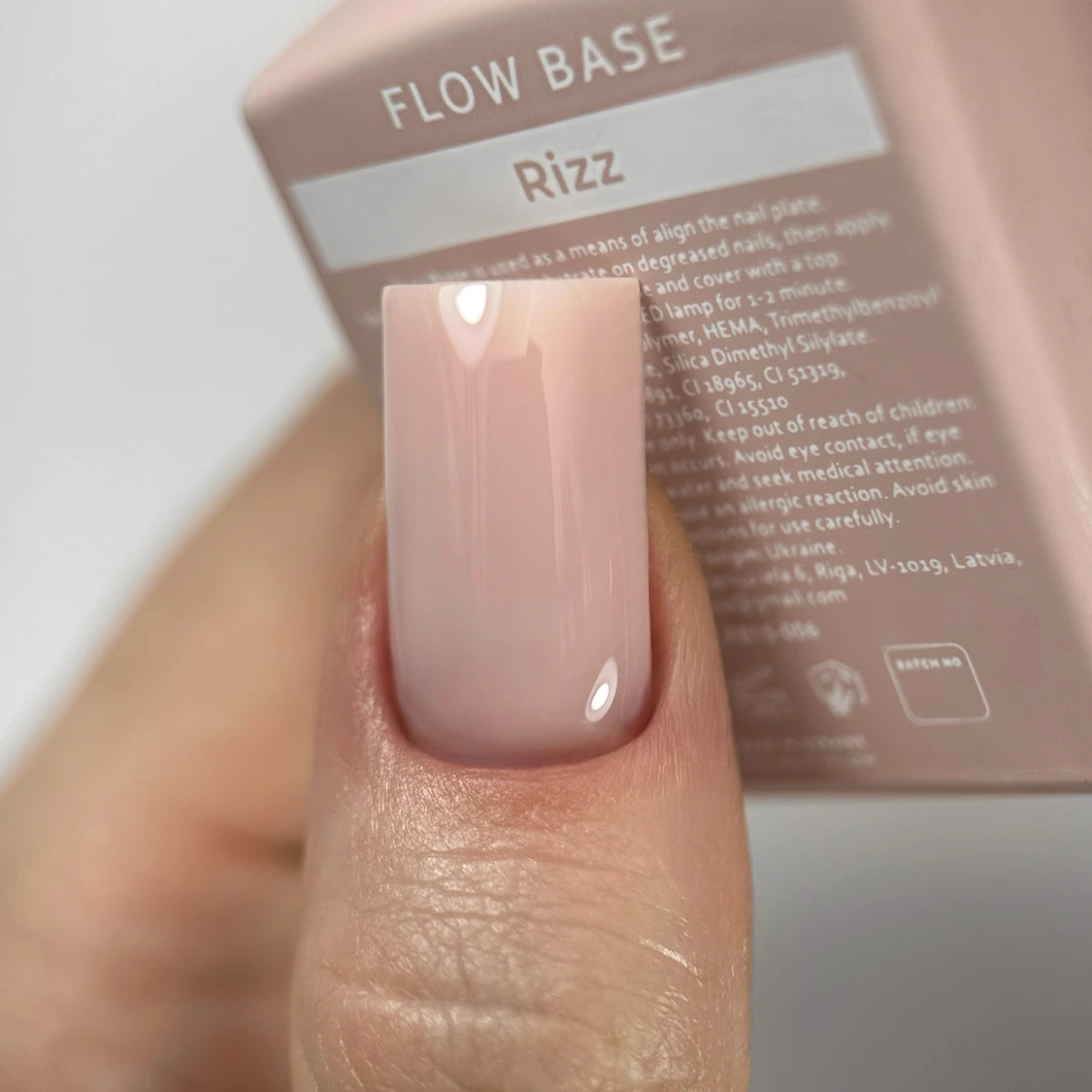 Close-up of a fingernail with glossy nude pink gel polish and a Rizz Flow Base nail product box