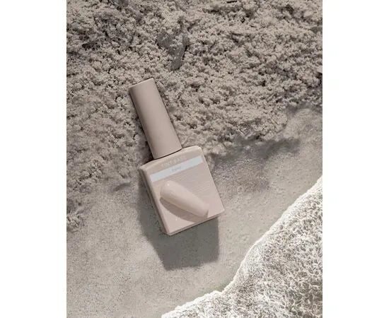 Beige gel nail polish bottle with matching swatch on sandy textured background