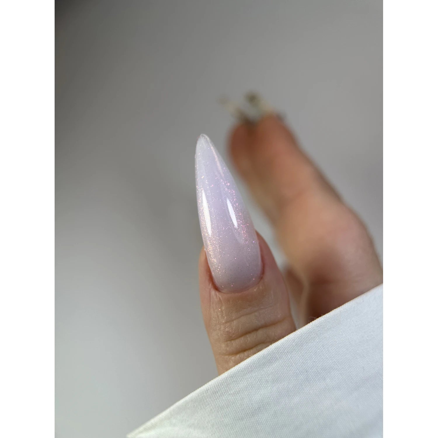 Hand with long almond-shaped nail featuring shimmery light pink gel polish manicure