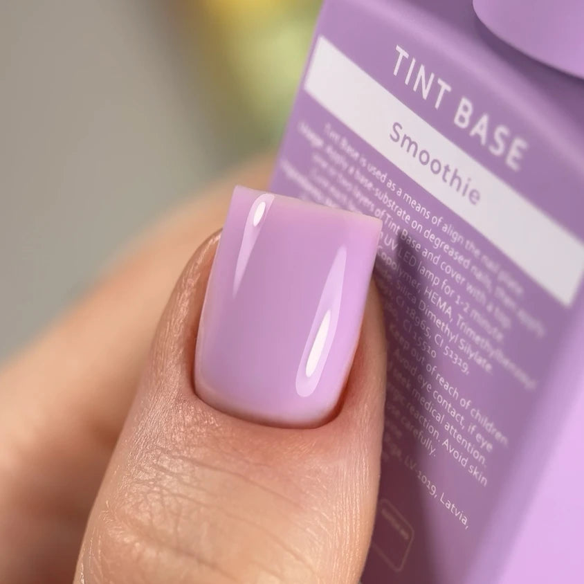Close-up of a thumb with glossy pastel purple gel nail polish, manicure product in background