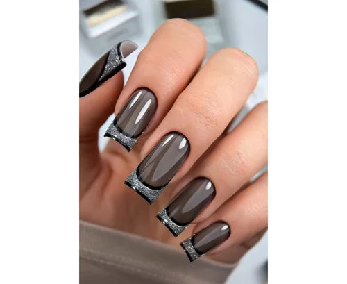 Hand with glossy black and gray coffin-shaped nails with silver glitter tips, manicure design
