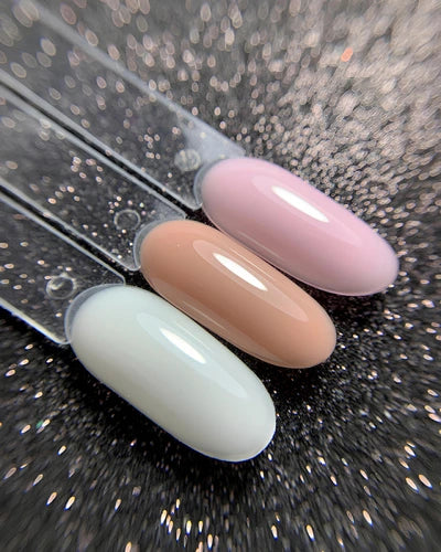 Three nail color swatches in milky white, nude, and soft pink on a glitter background