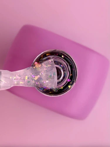 Clear nail polish with iridescent glitter flakes in a pink square bottle, top view