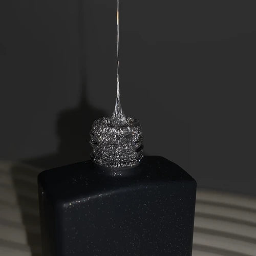 Silver glitter UV gel polish being pulled from a black bottle for manicure nail art