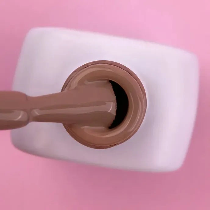 Close-up of nude brown gel nail polish bottle and brush on pink background