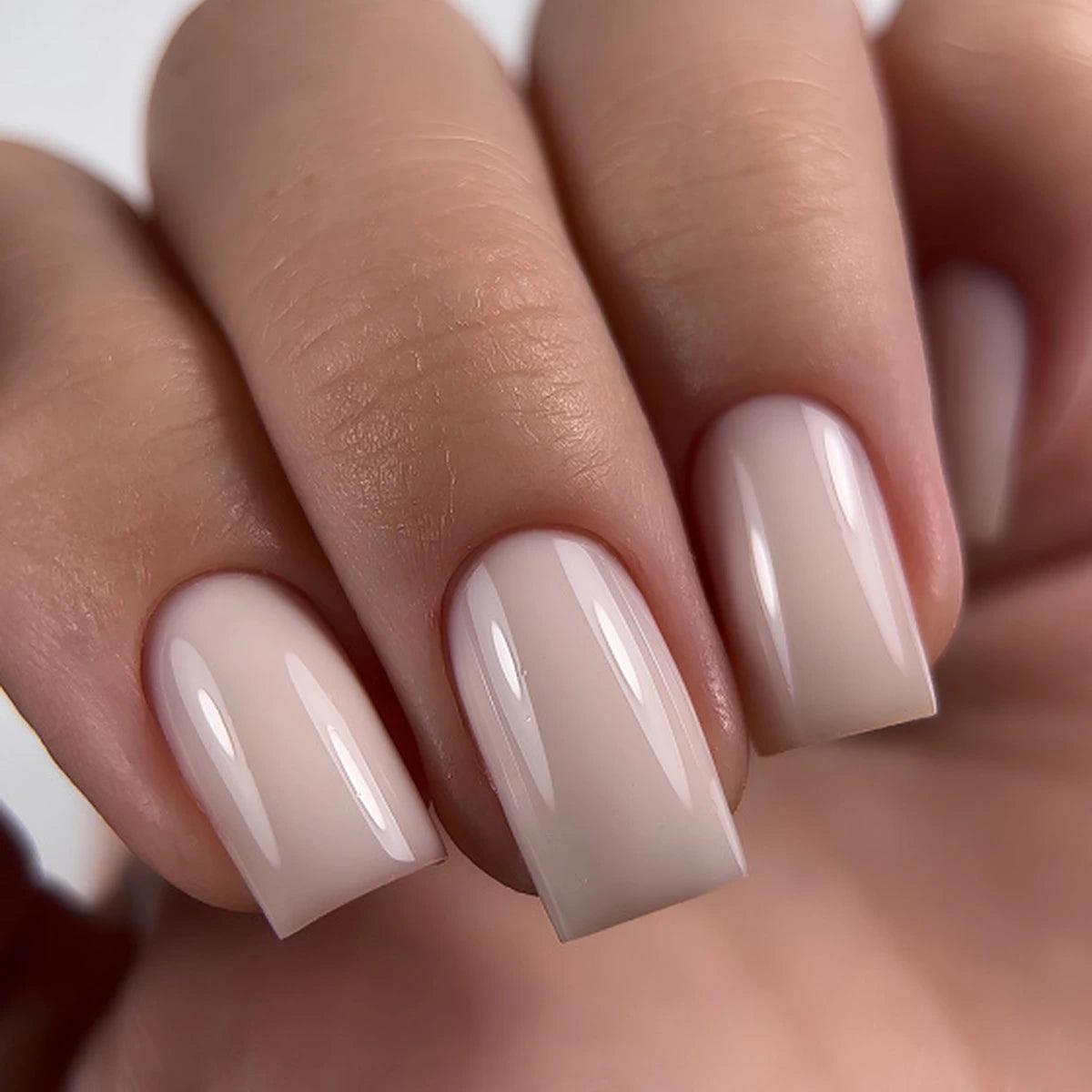 Close-up of a hand with neatly manicured square-shaped nails painted in a glossy, soft nude beige shade.