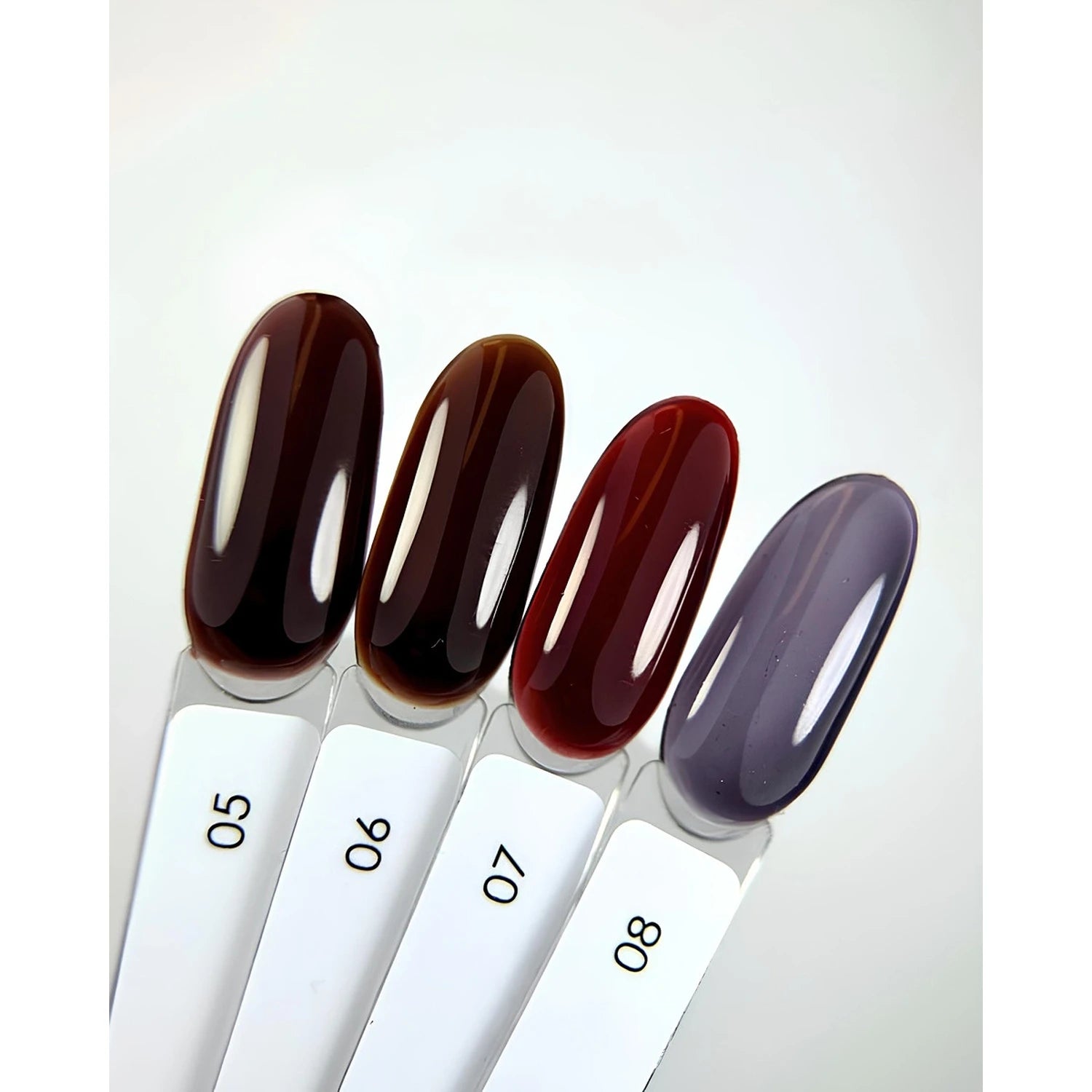 Four UV gel nail polish color samples in deep brown, red, and gray shades on display sticks